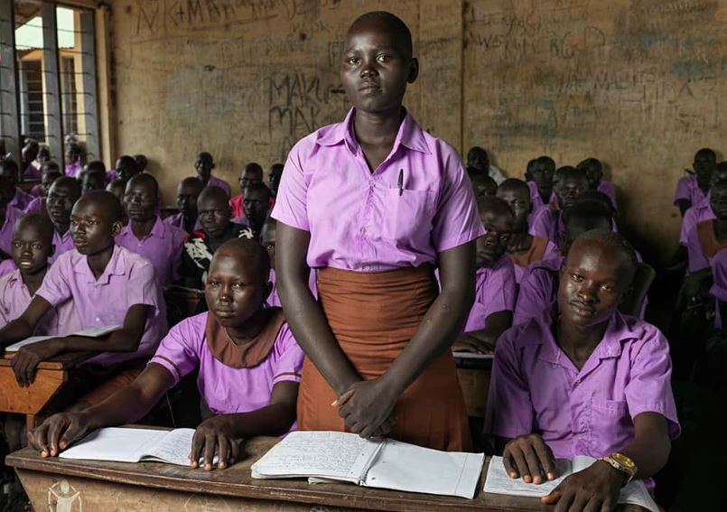 Hellena stands in her classroom in South Sudan. “[When my family and I] eat only once a day, in the evening,” she says. “But in the morning and lunch time, we don’t eat. … we eat pumpkin leaves, it’s the only plant that survived the drought, but it doesn’t bear any fruit.”
